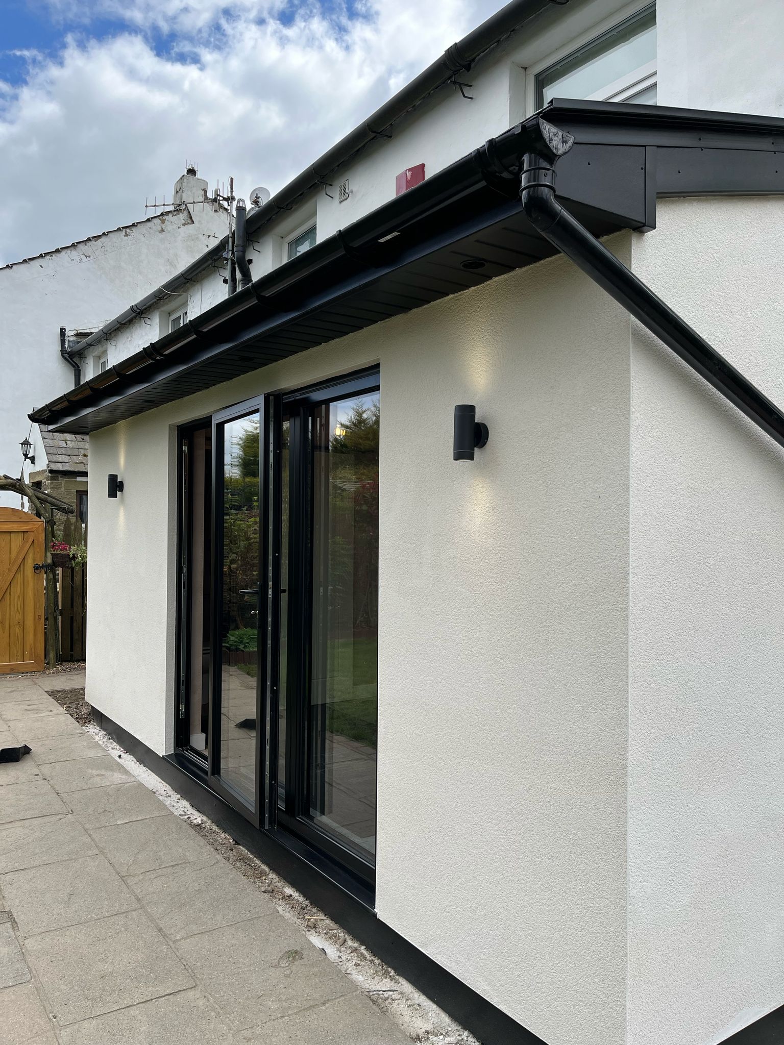Modern white rendered house extension with anthracite sliding doors and soffit lighting