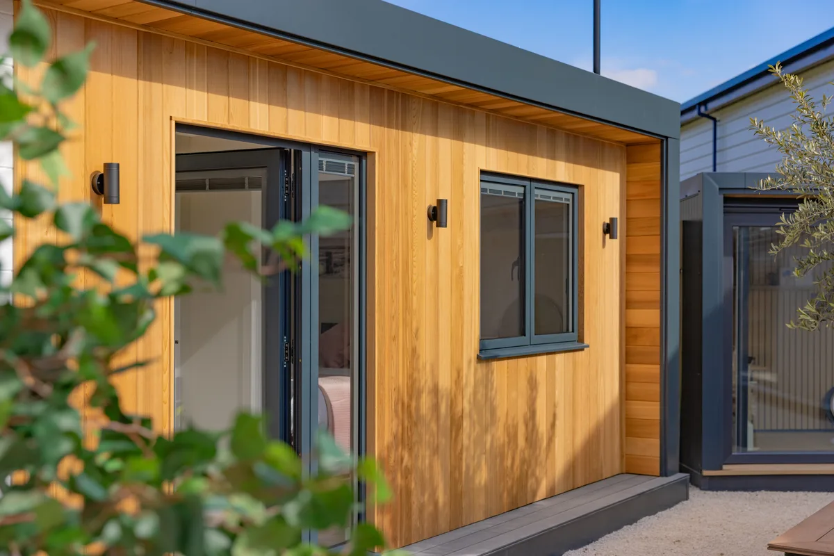 Cedar-clad bespoke SIP garden room with anthracite bifold doors and wall lights in Surrey