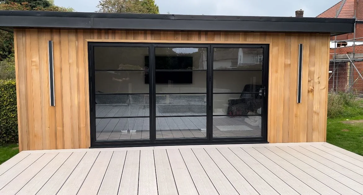 Cedar-clad garden room with slim-framed bifold doors opening onto composite decking, built by Helps & Co