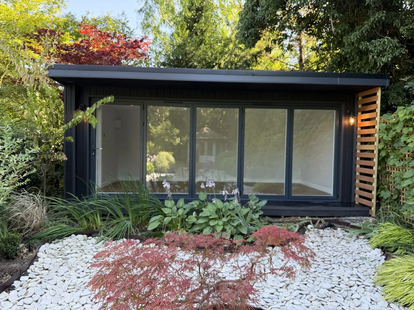 Dark-clad garden office set within a professionally landscaped Surrey garden with white cobbles and acers