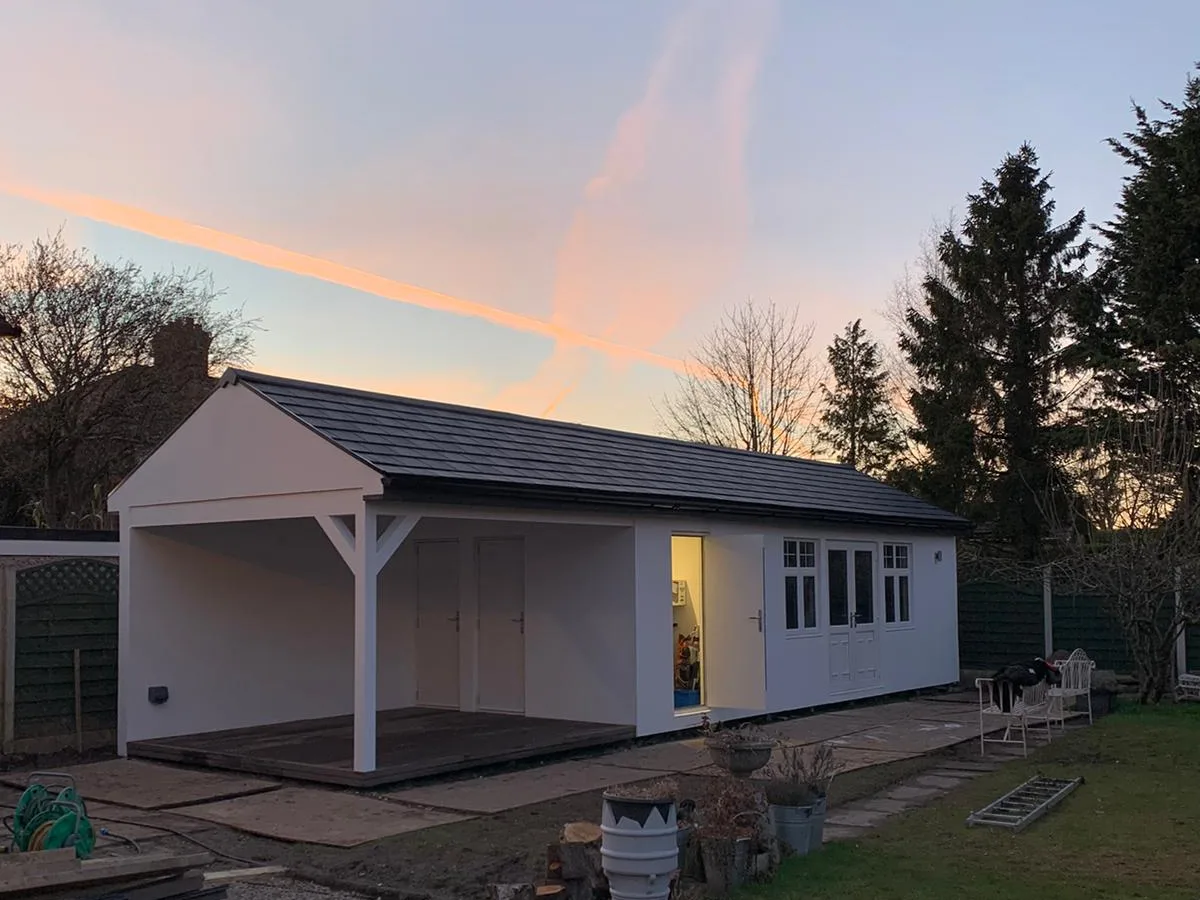 White garden studio with covered porch lit from inside at dusk, built by Helps & Co
