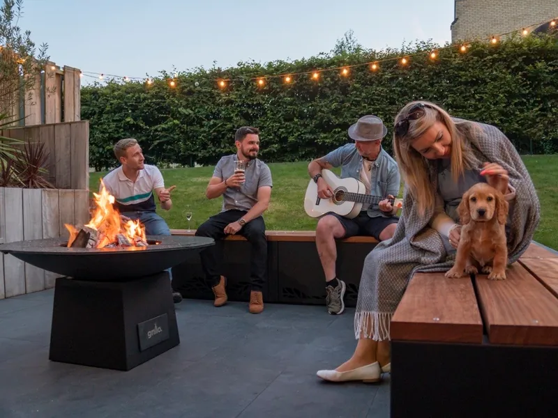 Friends relaxing around a Grillo fire pit in a Surrey garden at dusk