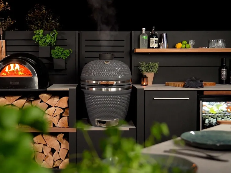 Grillo outdoor kitchen at dusk with a wood-fired pizza oven, kamado and log store