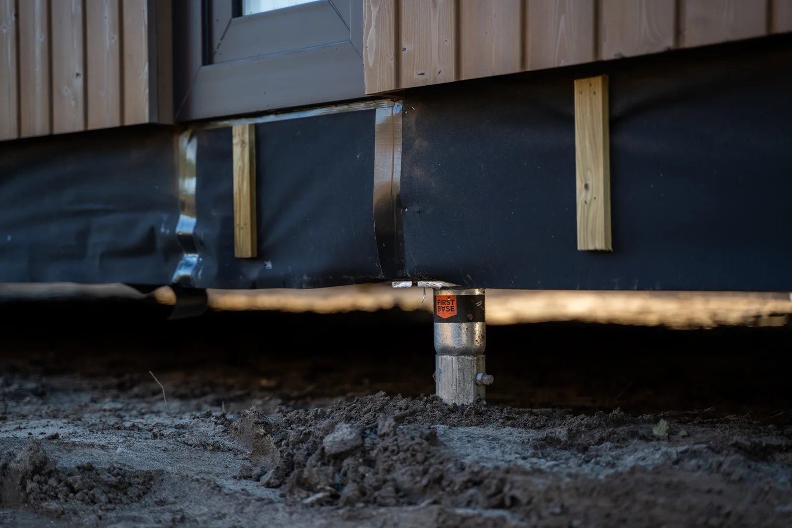 Ground screw supporting a finished timber-clad building with membrane detail visible