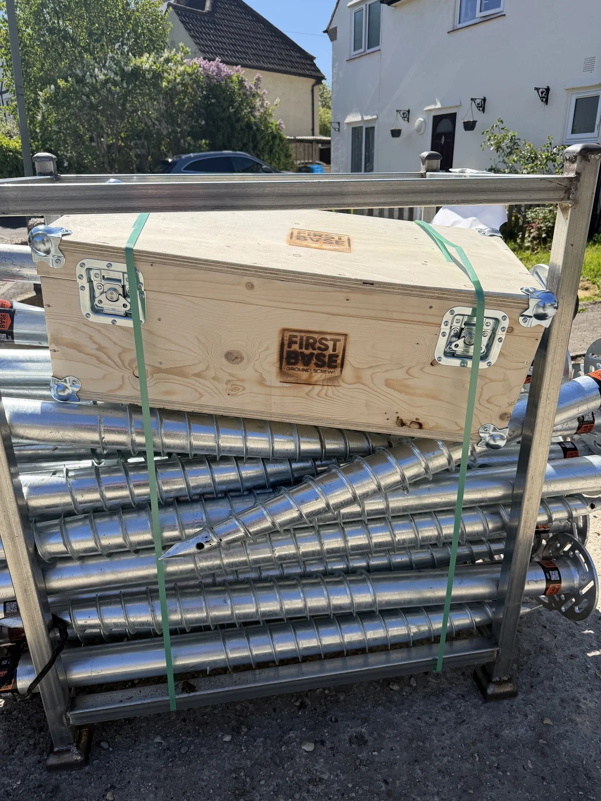 First Base ground screws stacked on a trolley with branded crate, ready for installation in Surrey
